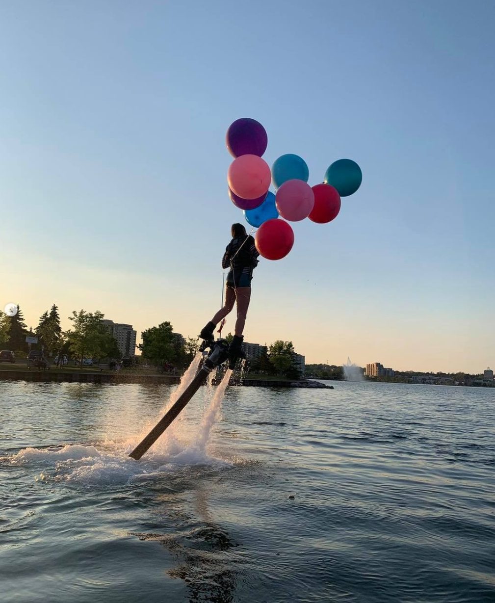 Flyboarder rising from the water holding a bunch of party balloons
