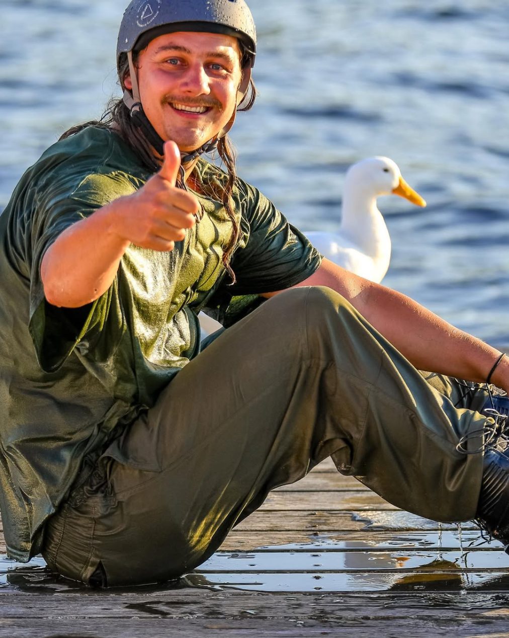 Chase Courneya giving a thumbs up on the dock beside a duck