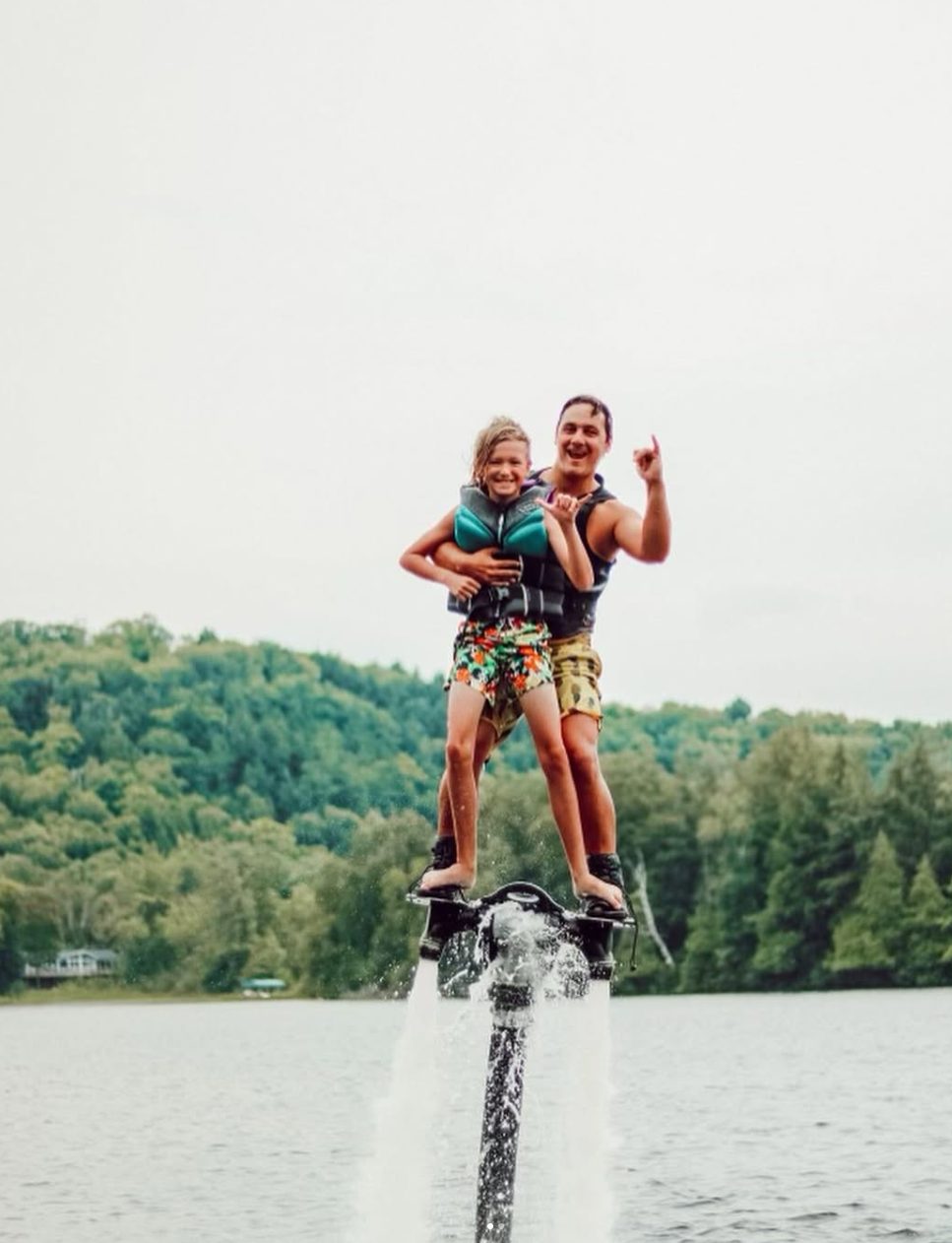 A parent and child flying together on a flyboard above the lake
