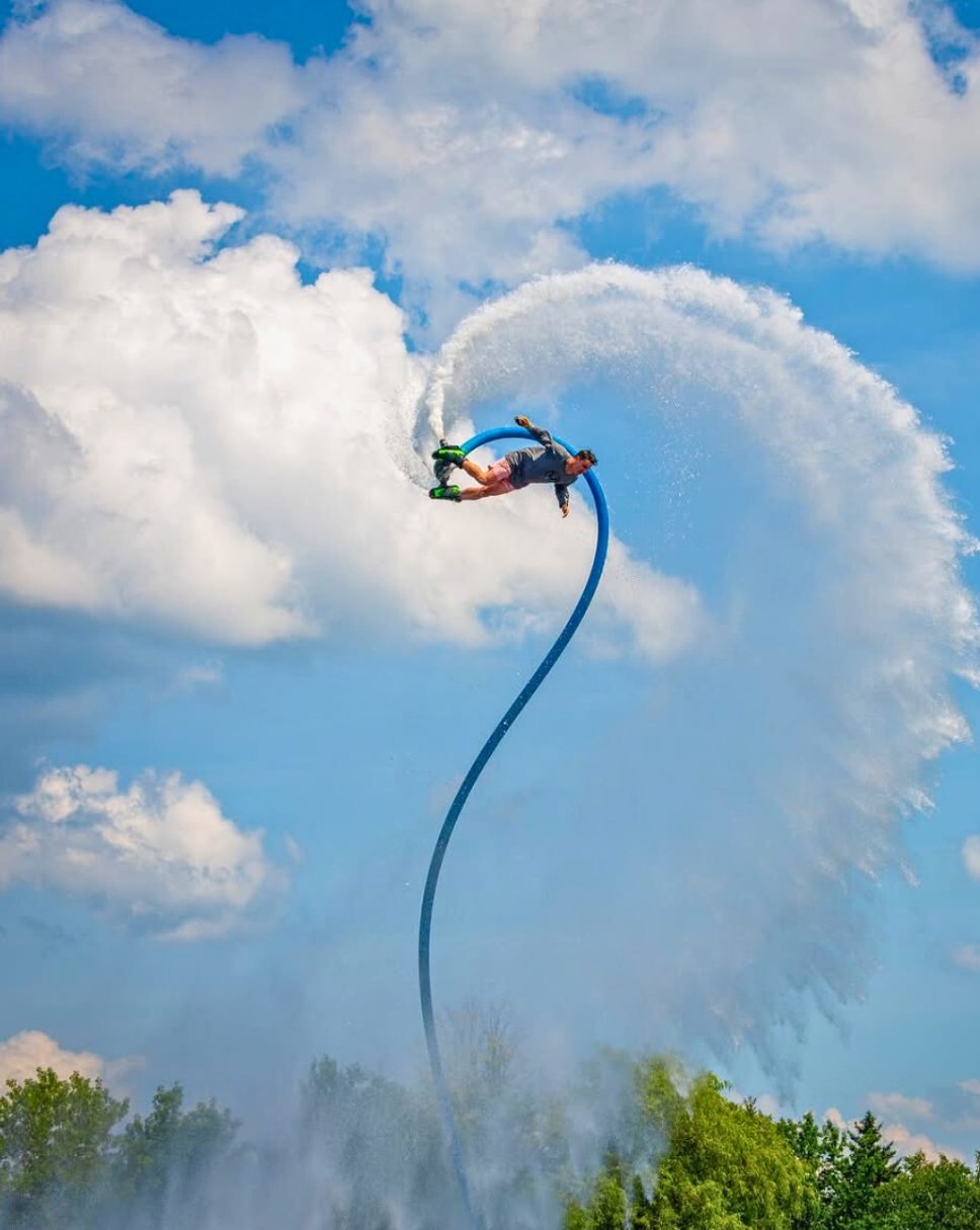 Flyboarder carving a huge arc of water across a blue sky