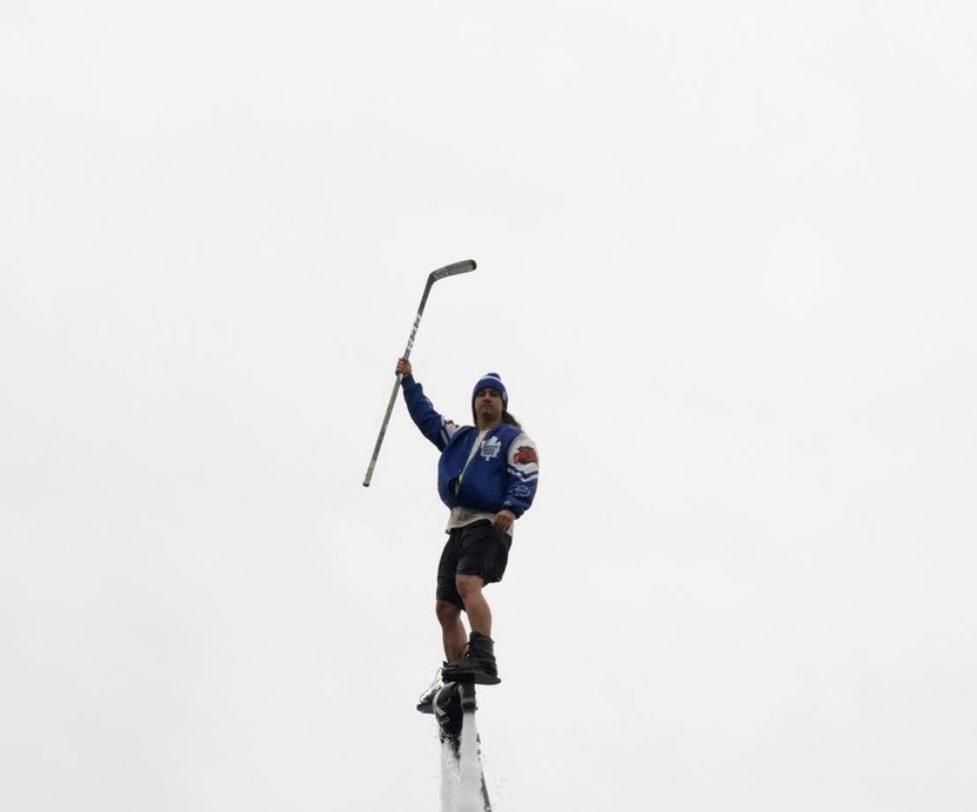 Flyboarder in a Maple Leafs jacket holding a hockey stick mid-air