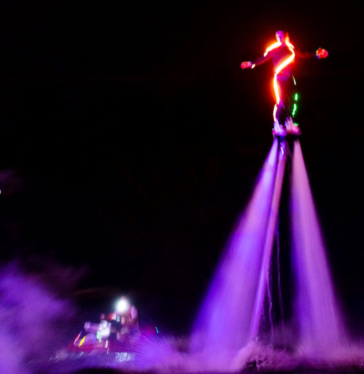 Flyboarder in a glowing LED suit performing at night