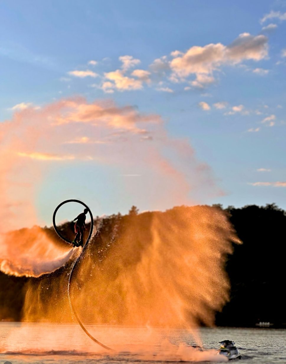 Flyboarder silhouetted in a loop of spray against a golden sunset
