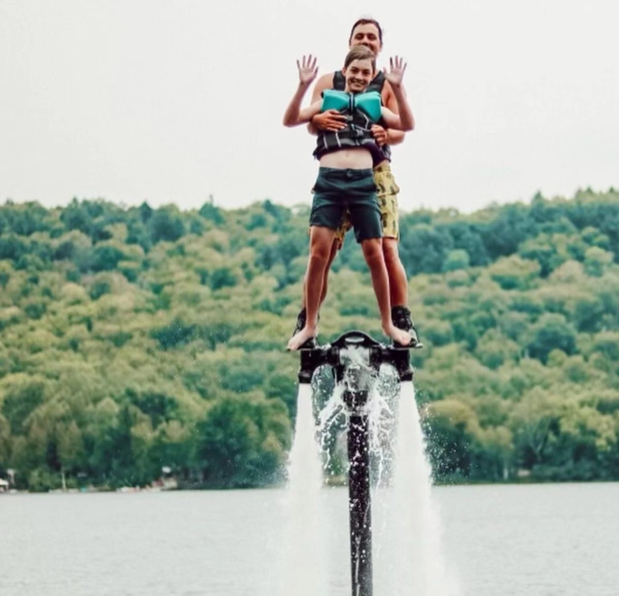 A parent and child standing together on a flyboard over the lake